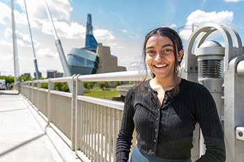 Student smiling as they stand at the start of a bridge in Winnipeg