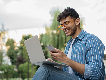 Student working outside on a laptop and phone