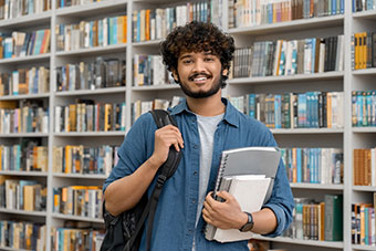A student smiling next to a bookshelf