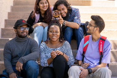 Five students sitting in the stairwell. Three in front and two at the back. One of the student is holding a bison doll.